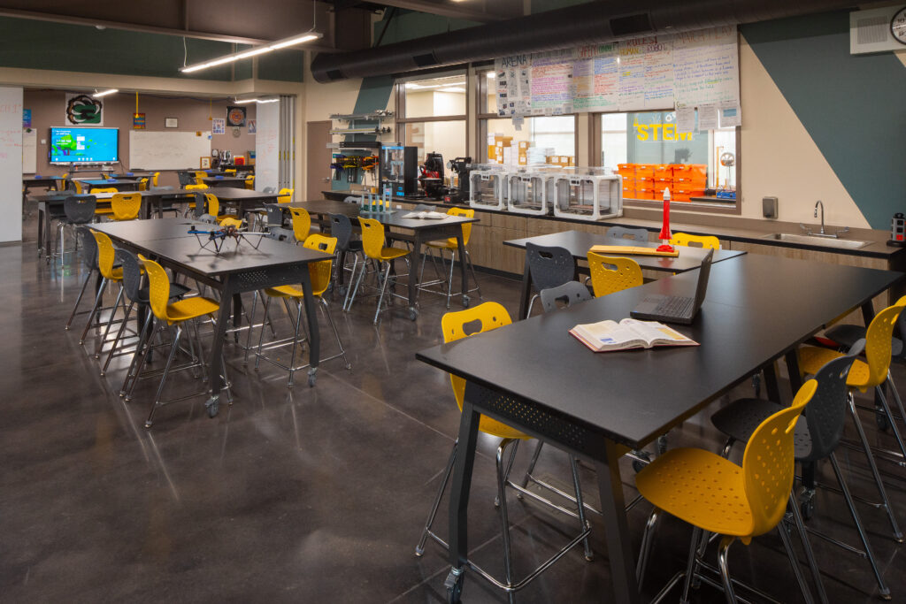 Interior of a modern STEM classroom at Greenfield High School with long tables, yellow chairs, and advanced educational equipment.