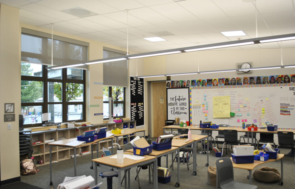 Inside a brightly lit modular classroom at Roosevelt Elementary School, featuring student desks, shelves, and large windows.