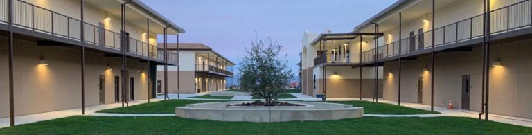 Symmetrical view of the two modular buildings surrounding the Rancho Santana School courtyard, featuring a tree and greenery.
