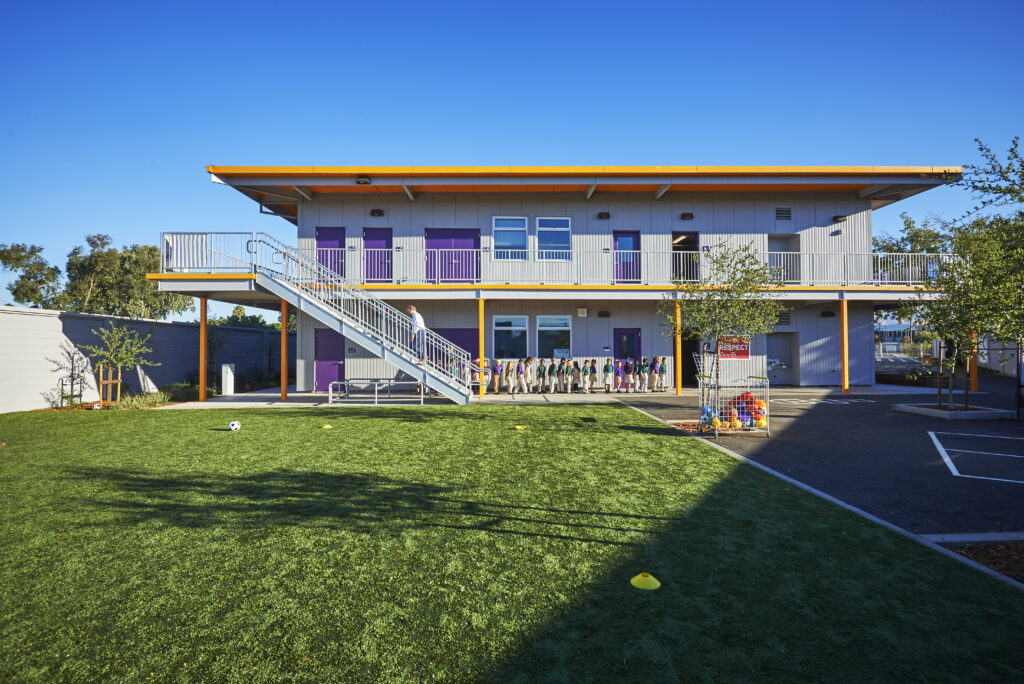 Rocketship Senter Road Campus playground with a two-story building in the background and students lined up outside.