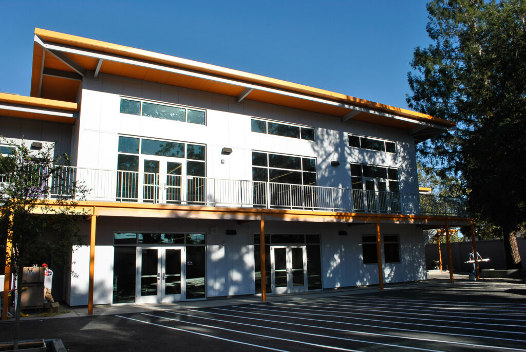 Exterior view of a two-story Rocketship school building, with orange accents and large windows, under a clear sky.