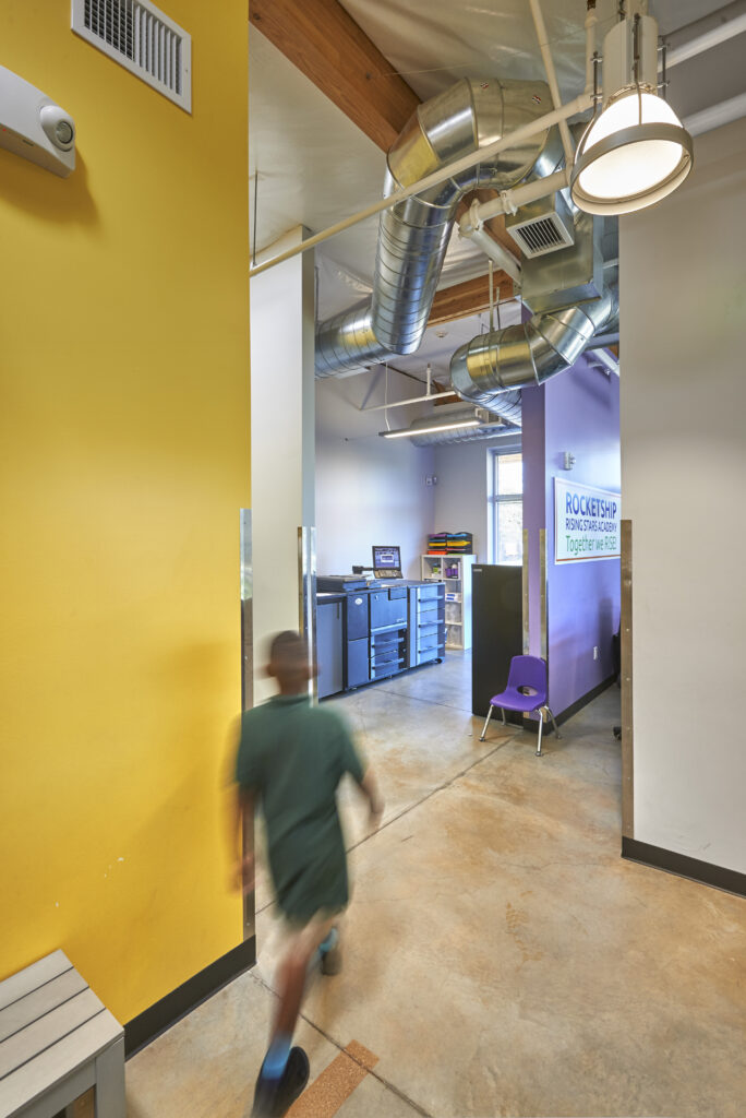 Rocketship school hallway with a student walking, showing HVAC ducts and a colorful interior.