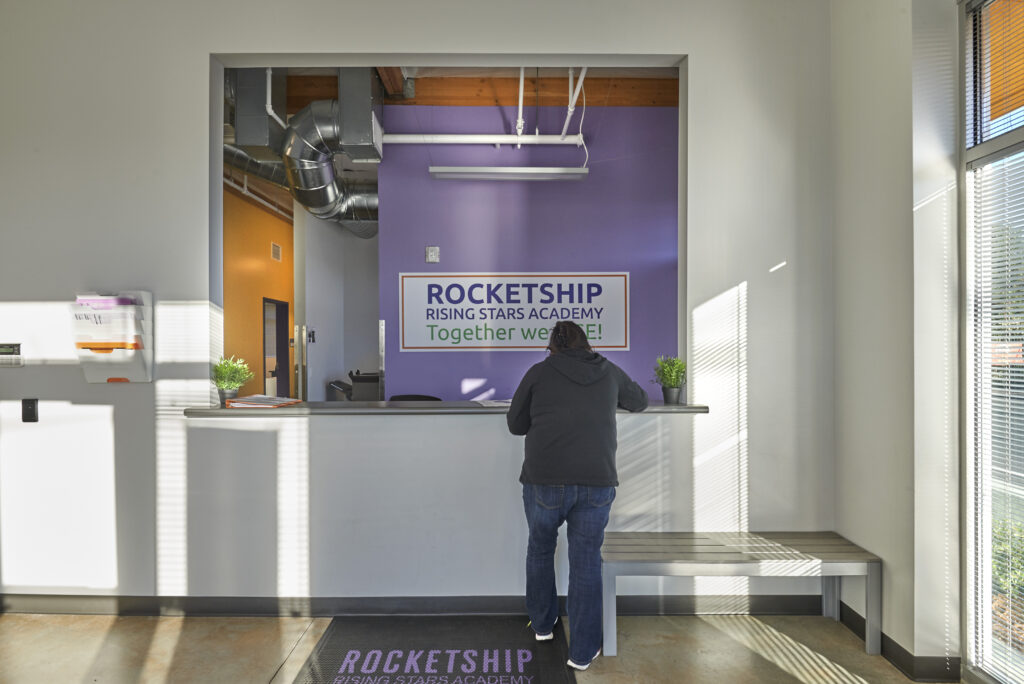 Reception area of Rocketship Rising Stars Academy, with a staff member assisting a visitor at the counter.