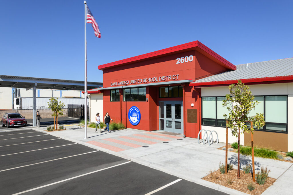 The prominent red facade and official entrance of the San Leandro Unified School District headquarters, featuring professional landscaping and clear district branding.